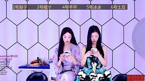 Media: Video of two Asian women in stylish outfits, seated at a futuristic table with a hexagonal patterned background. They focus intently on smartphones.