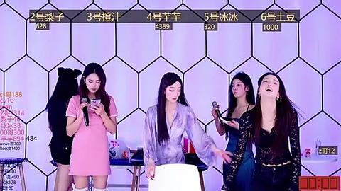 Media: Video of four women, three singing into microphones, standing against a hexagonal patterned purple wall, wearing various outfits, including a pink dress, a white robe, and a black lace top.