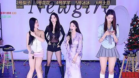 Media: Video of four Asian women in festive outfits singing into microphones on stage, surrounded by holiday decorations, with a digital scoreboard and Chinese text in the background.