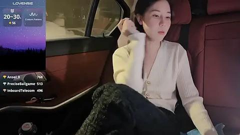 Media: Video of a woman with fair skin, dark hair, and wearing a beige cardigan, sitting in a car with a cityscape outside, showing live stream details on a phone screen.