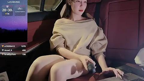 Media: Video of a young woman with fair skin, long brown hair, and red lipstick, wearing a loose beige sweater, sitting in a car at night.