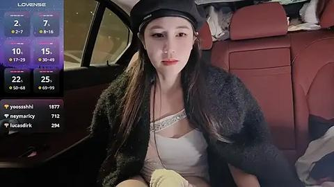 Media: Video of a young East Asian woman with long black hair, wearing a black hat, black fur coat, and white lace top, seated in a red leather car seat at night.