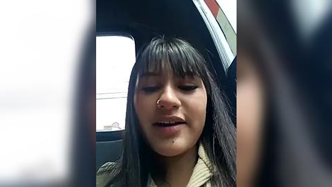 Media: Video of a young woman with long dark hair, wearing a green jacket, sitting in a car, looking down, possibly in distress.