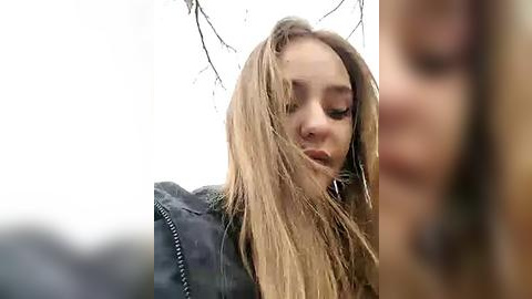 Media: Video of a young woman with long, wet blonde hair, wearing a black leather jacket, standing outdoors against a blurred, snowy landscape.