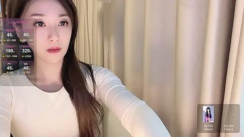 Media: A video of a young East Asian woman with long, straight brown hair, wearing a white long-sleeved top, standing in front of beige curtains. The image includes a live streaming overlay with chat and viewer statistics.