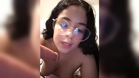 Media: Video of a topless, fair-skinned woman with curly black hair and blue-tinted glasses, leaning in close to a man's erect penis.