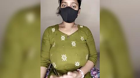 Media: Video of a South Asian woman with medium brown skin, wearing a black mask, olive-green kurta with white floral embroidery, and a pink and purple dupatta. Background is blurry.