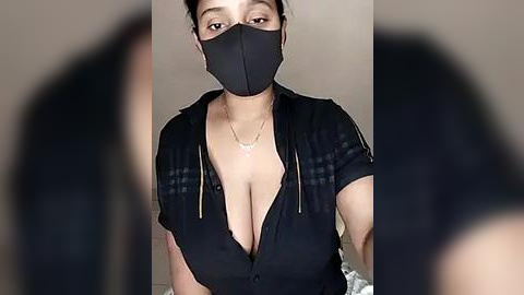 Media: A video of a woman with light brown skin, wearing a black face mask, black dress, and black hooded jacket, with her breasts partially exposed, in a blurred background.