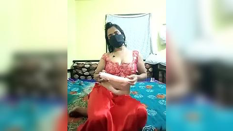 Media: A video shows a South Asian woman with dark hair and fair skin, wearing a red sari and black mask, holding a dildo, in a modest bedroom with a blue bedspread.