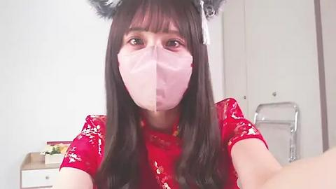 Media: Video of a young Asian woman with long black hair, wearing a red floral dress, cat ear headband, and pink face mask indoors.