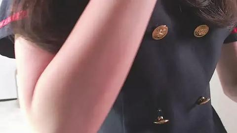 Media: A close-up video of a woman wearing a dark blue military-style uniform with gold buttons, showing off her well-toned, bare left arm.