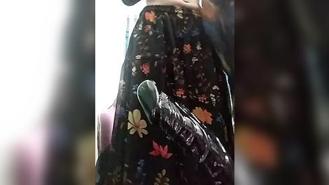 Media: A video captures a person holding a black, floral-patterned dress with a green purse, against a blurred, softly lit background.