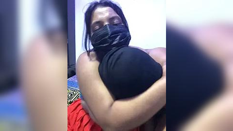 Media: Video of a person wearing a black mask, red shirt, and black headband, hugging a child, blurred background, showing a close, intimate moment.