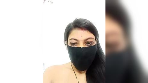 Media: Video of a young woman with long black hair, wearing a black mask, and a thin black necklace, against a plain white background.