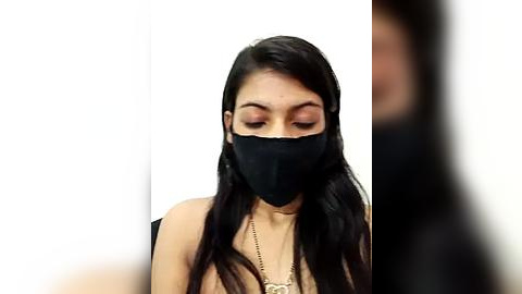 Media: A video of a young woman with long, straight black hair, wearing a black face mask and a gold necklace, standing against a plain white background.