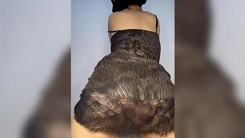 Media: Video of a woman's lower back and buttocks, wearing a short, black, sequined dress with a ruffled hem. She is viewed from behind, with a blurred figure in the foreground.