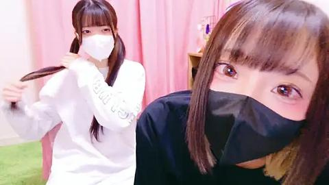 Media: Video of an East Asian woman with long, straight brown hair, wearing a white mask, white sweater, and black face mask, adjusting her hair in a pink room.