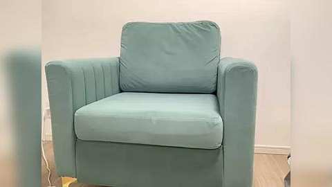 Media: Video of a mint-green, mid-century modern armchair with a plush, cushioned seat and backrest, resting against a plain white wall in a minimalist room with light wooden floors.