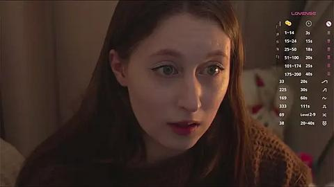 Media: A video of a fair-skinned woman with long brown hair, wearing a brown sweater, looking worried. In the background, a dimly lit room with a floral pillow.