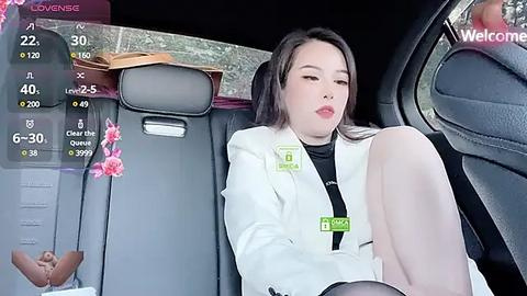 Media: Video of a young Asian woman with fair skin and long black hair, wearing a white jacket and black top, sitting in a car.