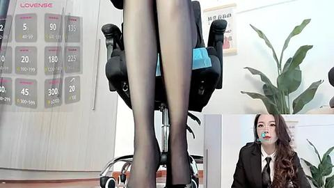 Media: Video of a woman's legs in sheer black tights, wearing a black suit, sitting in an office chair with a calendar behind. Inset: another woman with long hair and a black tie, mouth taped shut.