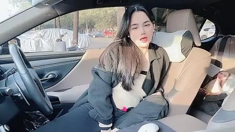 Media: Video of a young Asian woman with long black hair, red lipstick, wearing a black jacket and jeans, sitting in a beige leather car seat, with a baby in the backseat.