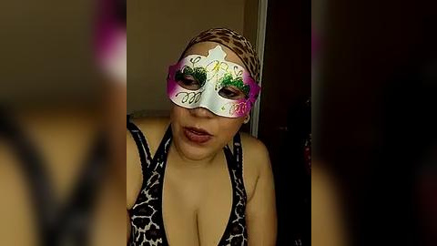 Media: A video of a light-skinned woman with medium-length hair, wearing a leopard-print dress and a decorative masquerade mask with green and pink designs, in a dimly lit indoor setting.