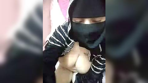 Media: Video of a person wearing a black balaclava and striped jacket, partially nude, with exposed breasts and genitals, blurred background.