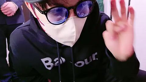 Media: Video of an Asian man in a black Burberry hoodie, wearing a mask, glasses, and waving, with blurred background.