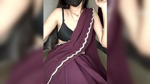 Media: Video of a South Asian woman in a black bra, maroon sari with white lace trim, black mask, and black gloves, sitting indoors with blurred background.