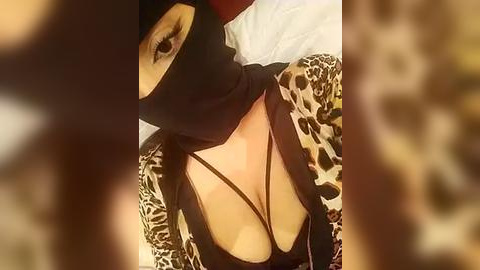 Media: Video of a woman wearing a black mask with an eye cutout, a black strappy top, and a leopard print jacket, partially obscured by a blurred, brown background.