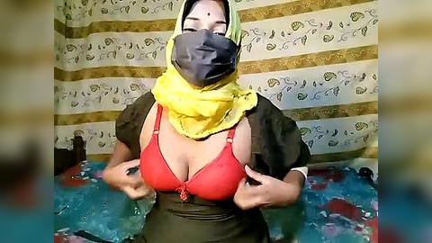 Media: Video of a woman with light skin, wearing a red bra, yellow headscarf, and black mask in a colorful room with patterned curtains.