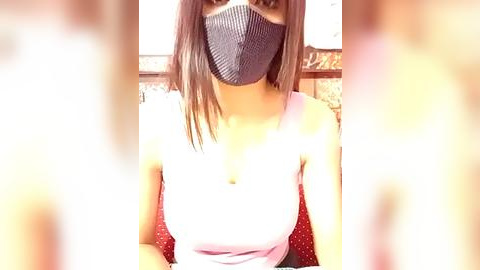 Media: Video of a woman with medium-length brown hair, wearing a gray face mask, pink tank top, and red polka-dot patterned chair.