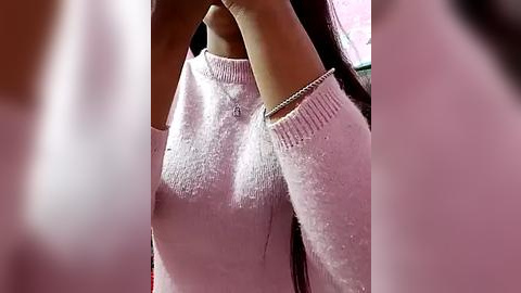 Media: A close-up video of a woman with long, dark hair wearing a pink, textured sweater, revealing her nipples through the fabric. The image is blurry, focusing on the sweater and chest area.