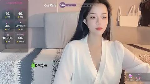 Media: Video of an East Asian woman with long black hair, fair skin, and red lipstick, wearing a white blouse. Background shows a modern bedroom with a striped bedspread and a white wall.