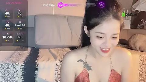 Media: Video of an East Asian woman with long black hair, wearing a red halter top, sitting on a bed with a beige blanket. She has a tattoo of a dragon on her shoulder. A virtual reality display shows a game interface in the background.