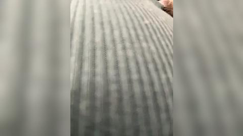 Media: Video of a textured, ribbed, grey carpet surface with blurred vertical lines, partially showing a person's arm and hand in the top right corner.