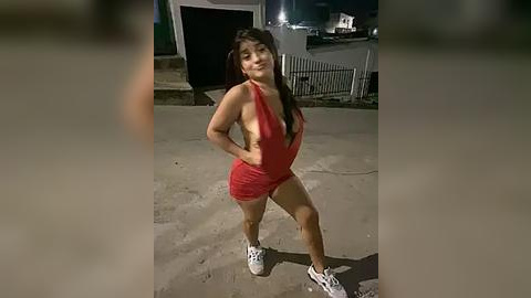 Media: Video of a pregnant woman with long dark hair in a revealing red halter top and shorts, standing outside at night, smiling.