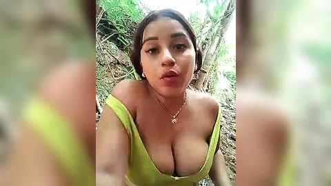 Media: A video of a young woman with light brown skin and dark hair, wearing a lime green off-shoulder top, posing outdoors in a forested area with blurred trees.