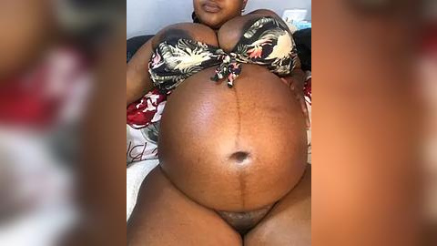 Media: Video of a heavily pregnant Black woman wearing a floral bikini top, revealing her large belly and dark skin. The background is blurred.