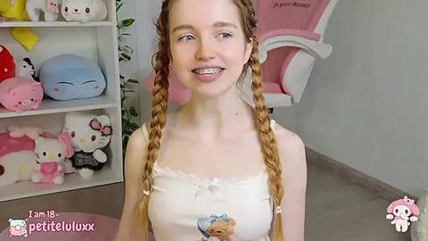 Media: Video of a young, pale-skinned woman with long, blonde braided pigtails, wearing a white tank top with a Hello Kitty design, smiling with braces. Background includes Hello Kitty-themed shelves and a pink chair.