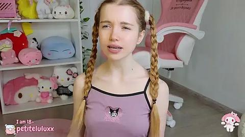 Media: A video of a young Caucasian woman with fair skin and long, blonde pigtails, wearing a pink tank top with a black cat design. She's in a pink gaming chair in a room filled with Hello Kitty-themed decor.