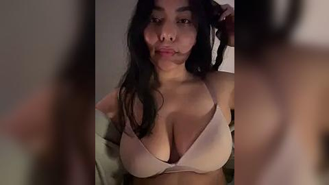 Media: Video of an Asian woman with long black hair, wearing a beige bra, smiling and licking her lips, blurred background, dim lighting.