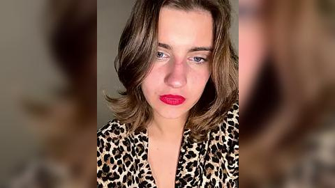 Media: Video of a young woman with shoulder-length brown hair, fair skin, and red lipstick, wearing a leopard print dress, against a blurred background.