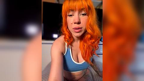 Media: Video of a young woman with vibrant orange hair, fair skin, and a blue sports bra, leaning forward, showing tattoos on her arms.