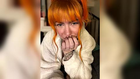 Media: Video of a pale-skinned woman with bright orange hair and bangs, wearing a white fur-trimmed coat, looking distressed and biting her nails. Background is blurred, suggesting an indoor setting.