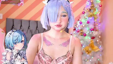 Media: Video of a light-skinned woman with blue hair, wearing a pink lace camisole, adorned with floral tattoos. She stands in front of a festive, colorful Christmas tree in a cozy room with striped walls.