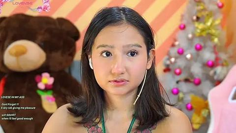 Media: A video of a young Asian woman with straight black hair, wearing headphones, in a festive room with a Christmas tree and plush bear.