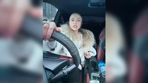 Media: Video of a woman with a shaved head and light skin, wearing a white fur-trimmed coat, driving a car with a black steering wheel.