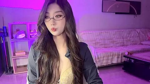 Media: Video of an East Asian woman with long black hair, wearing glasses, a black jacket, and a revealing lace bra, standing in a dimly-lit, cozy living room with purple lighting.